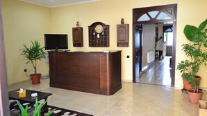 A living room with a wooden entertainment center, a flat-screen TV, a large clock, and potted plants. - Porto Franco Residence (Braila)