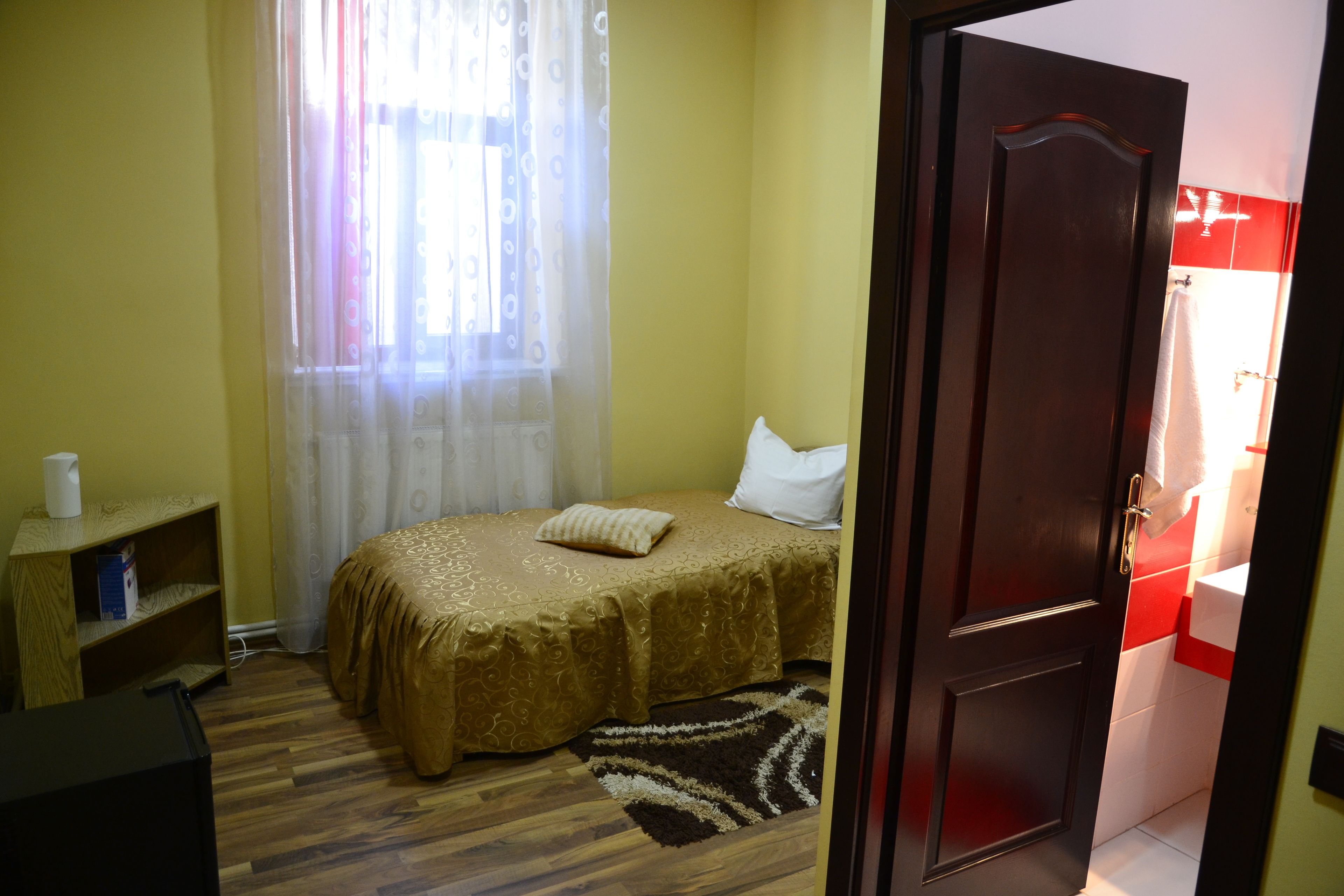 A bedroom with a bed, a bedside table, a shelf, and a door leading to a bathroom.