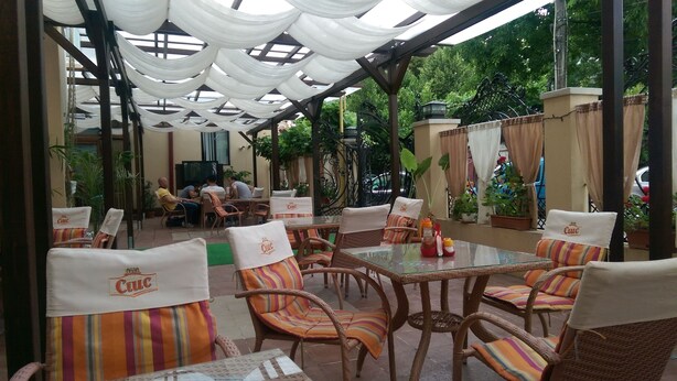 An outdoor patio area with wicker furniture and striped cushions, featuring a glass table and white drapes overhead. - Porto Franco Residence (Braila)
