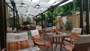 An outdoor patio area with wicker furniture and striped cushions, featuring a glass table and white drapes overhead. - Porto Franco Residence (Braila)