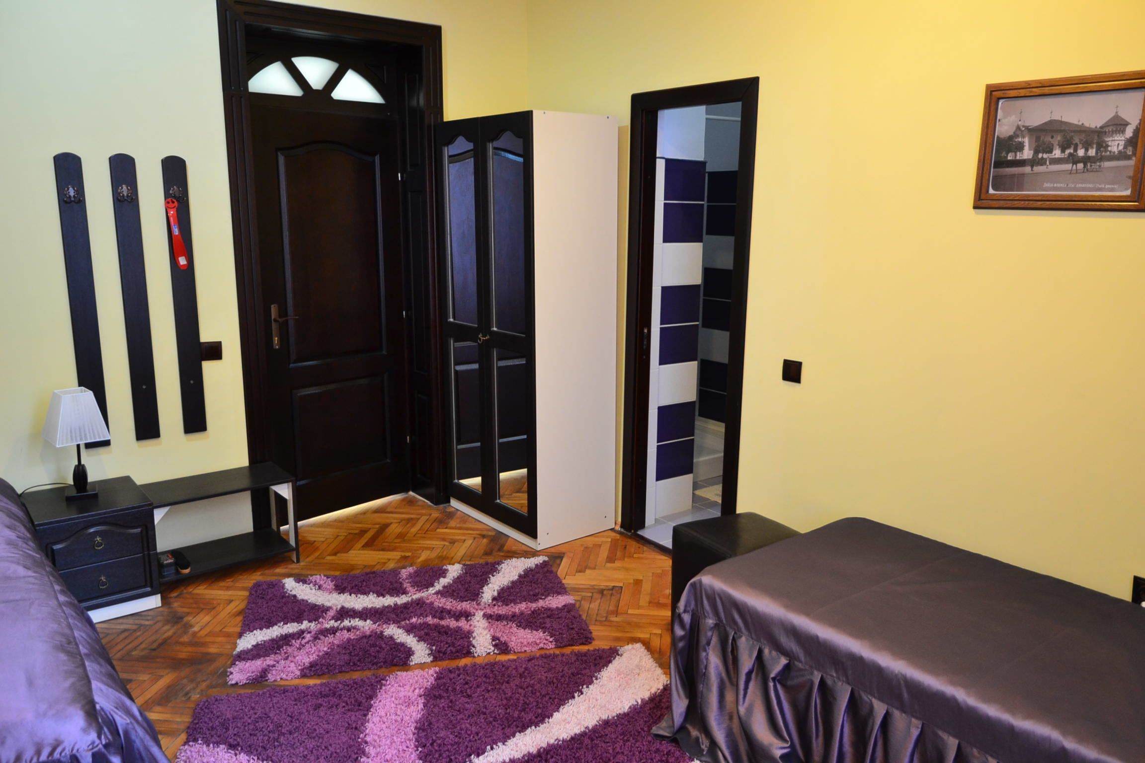 A room with a bed, a desk, a chair, a mirror, and a door.