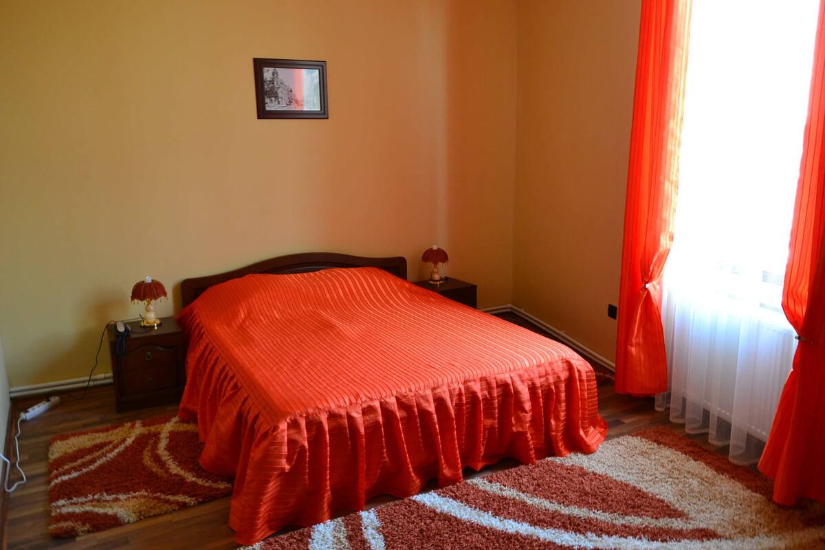 A bedroom with a large bed, a nightstand with a lamp, and a picture on the wall.