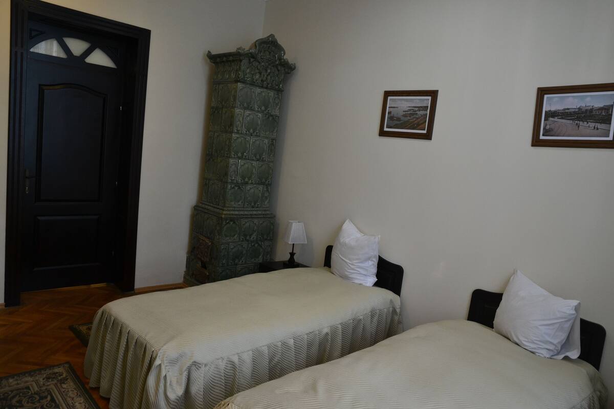 A room with two beds, a stone fireplace, a door, and two framed pictures on the wall.