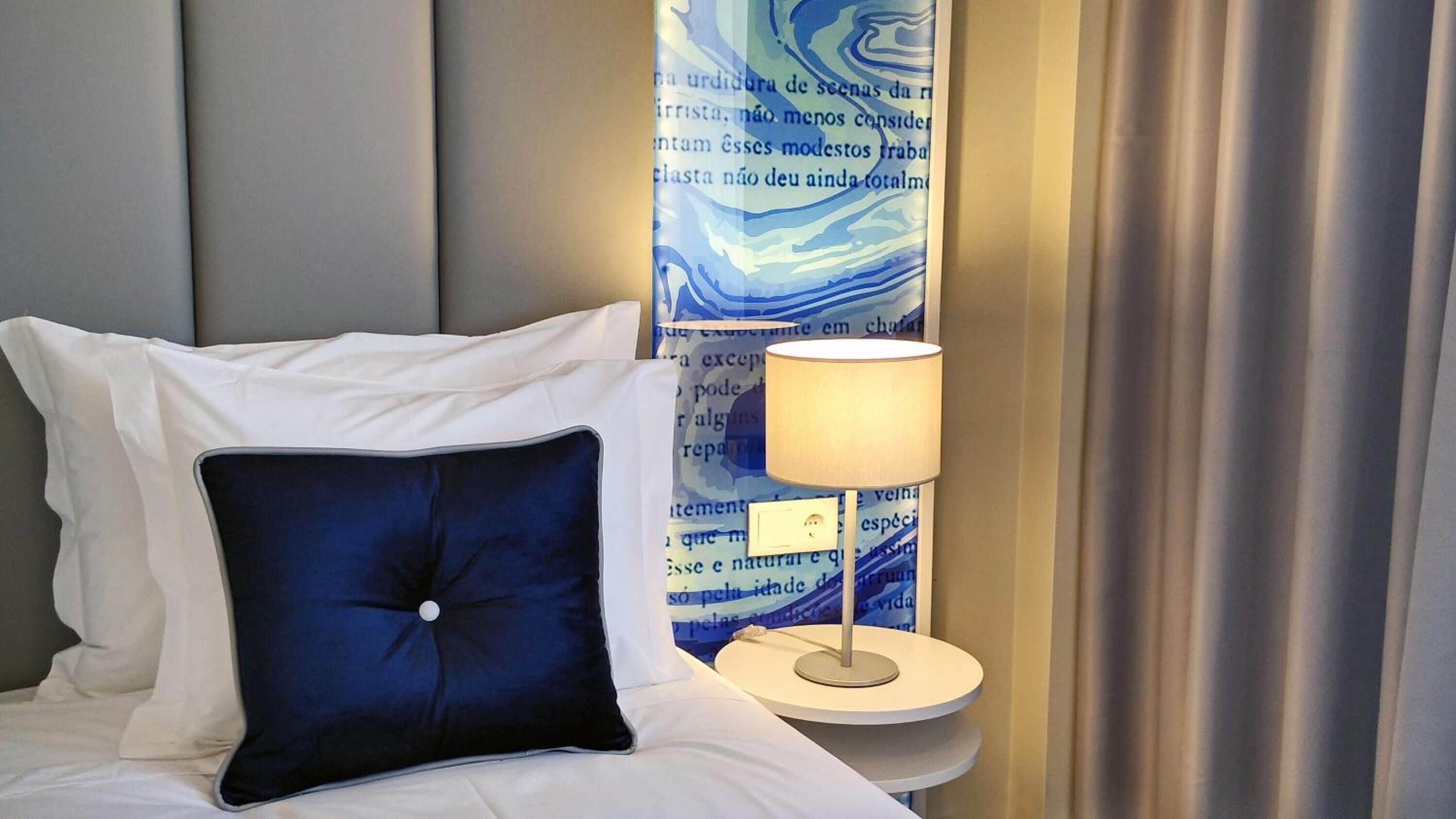Ein Hotelzimmer mit einem Bett, einem blauen Kopfkissen, einer Nachttischlampe und einer Wand mit einem blauen, abstrakten Muster.