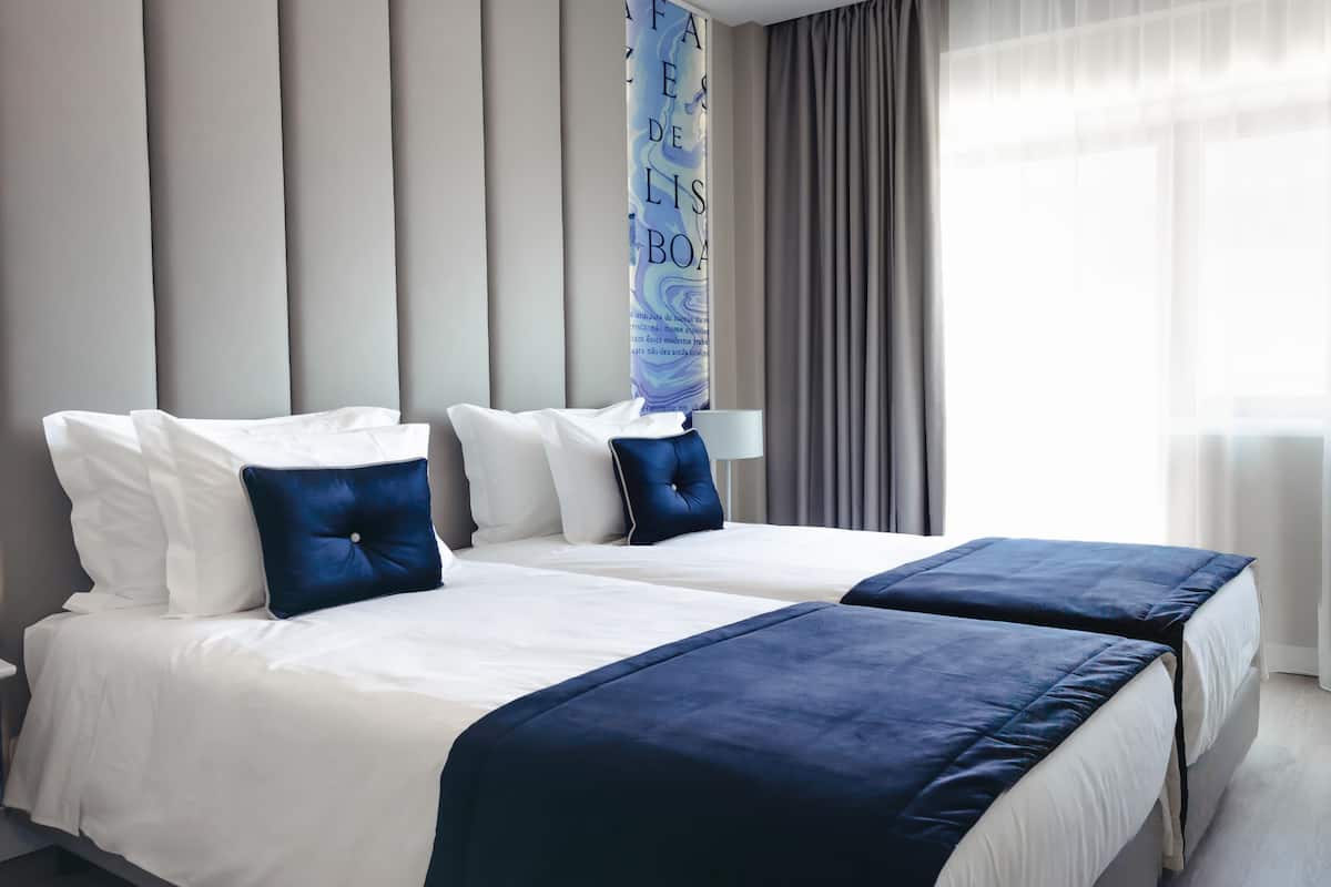 Ein Hotelzimmer mit zwei Betten, einem großen Fenster mit Vorhängen und einer Wand mit vertikalen Paneelen.