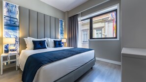 Una habitación de hotel con cama, mesita de noche, ventana con cortinas y una pared decorada con obras de arte.
