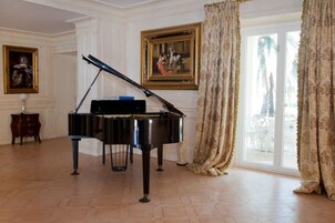 Un pianoforte a coda in una stanza ampia con una grande finestra, un quadro appeso al muro e un tavolino di legno.