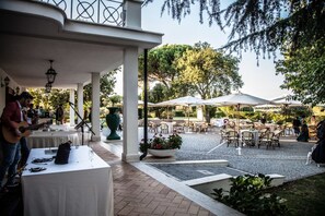 Un patio al aire libre con mesas y sillas, un músico tocando la guitarra y una fuente decorativa.