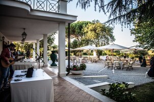 Un'area patio all'aperto con tavoli e sedie, un musicista che suona la chitarra e una fontana decorativa.