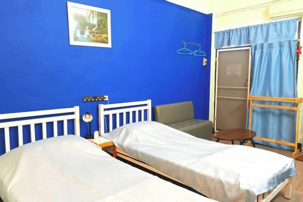 Une chambre avec deux lits simples, une petite table, une chaise et une armoire.