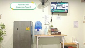 A room with a refrigerator, a water dispenser, a TV, and a small table with various items. - The Backpacker Station (Pak Kret)