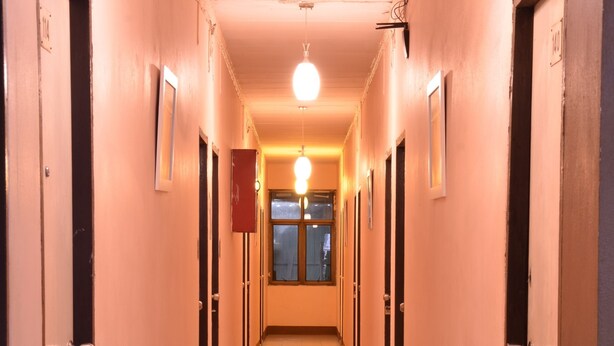 A long, narrow hallway with doors on both sides, leading to a room with a large window at the end. - The Backpacker Station (Pak Kret)