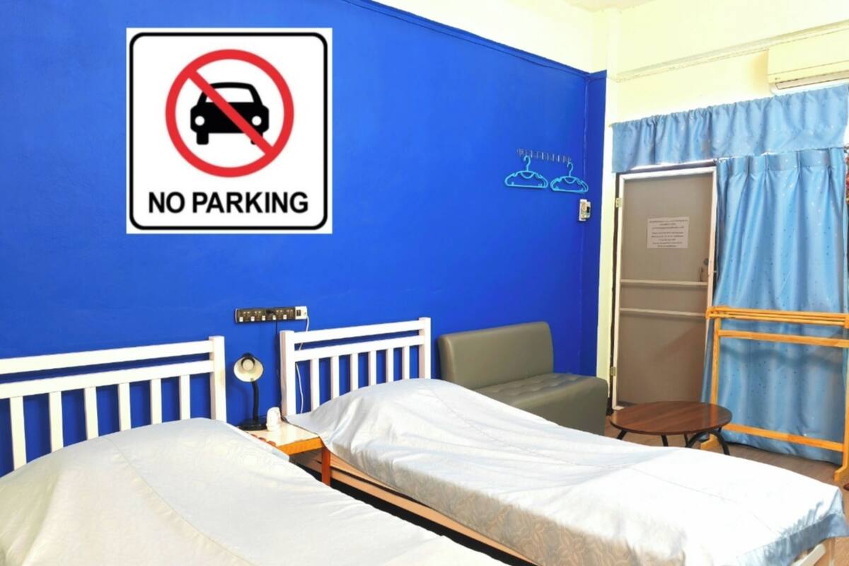 A hotel room with two beds, a 'NO PARKING' sign, a wardrobe, and a desk with a lamp.