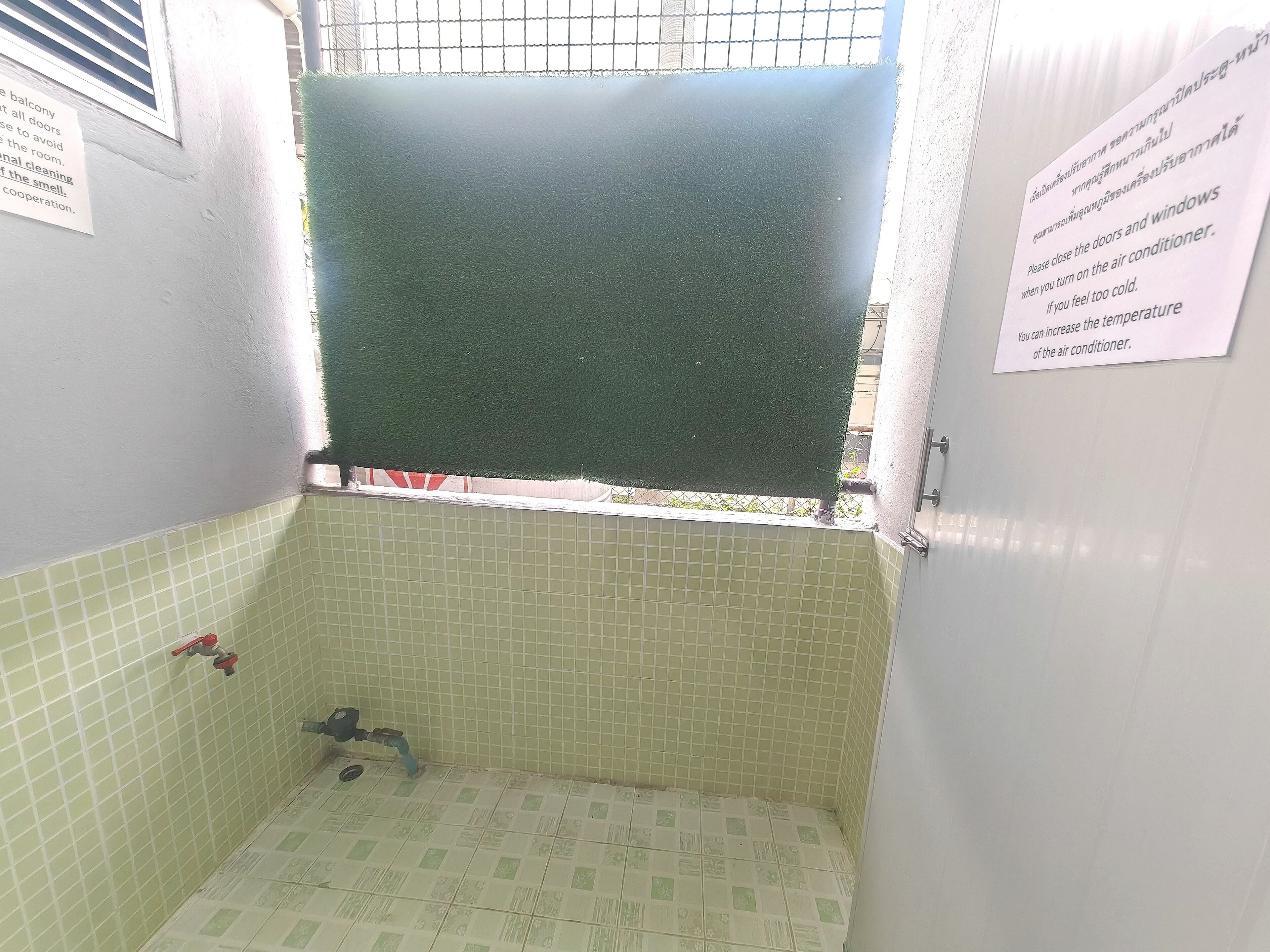 A small bathroom with a green shower curtain, a tiled floor, and a window with a metal grid.