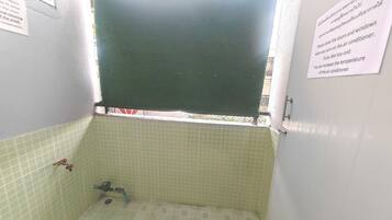 A small bathroom with a green shower curtain, a tiled floor, and a window with a metal grid.