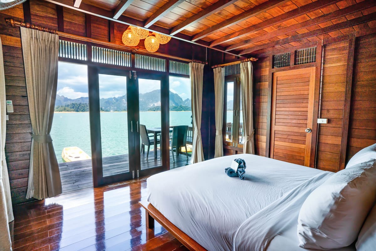 Ein Zimmer in einer Holzhütte mit einem Bett, Vorhängen und Blick auf einen See und Berge.