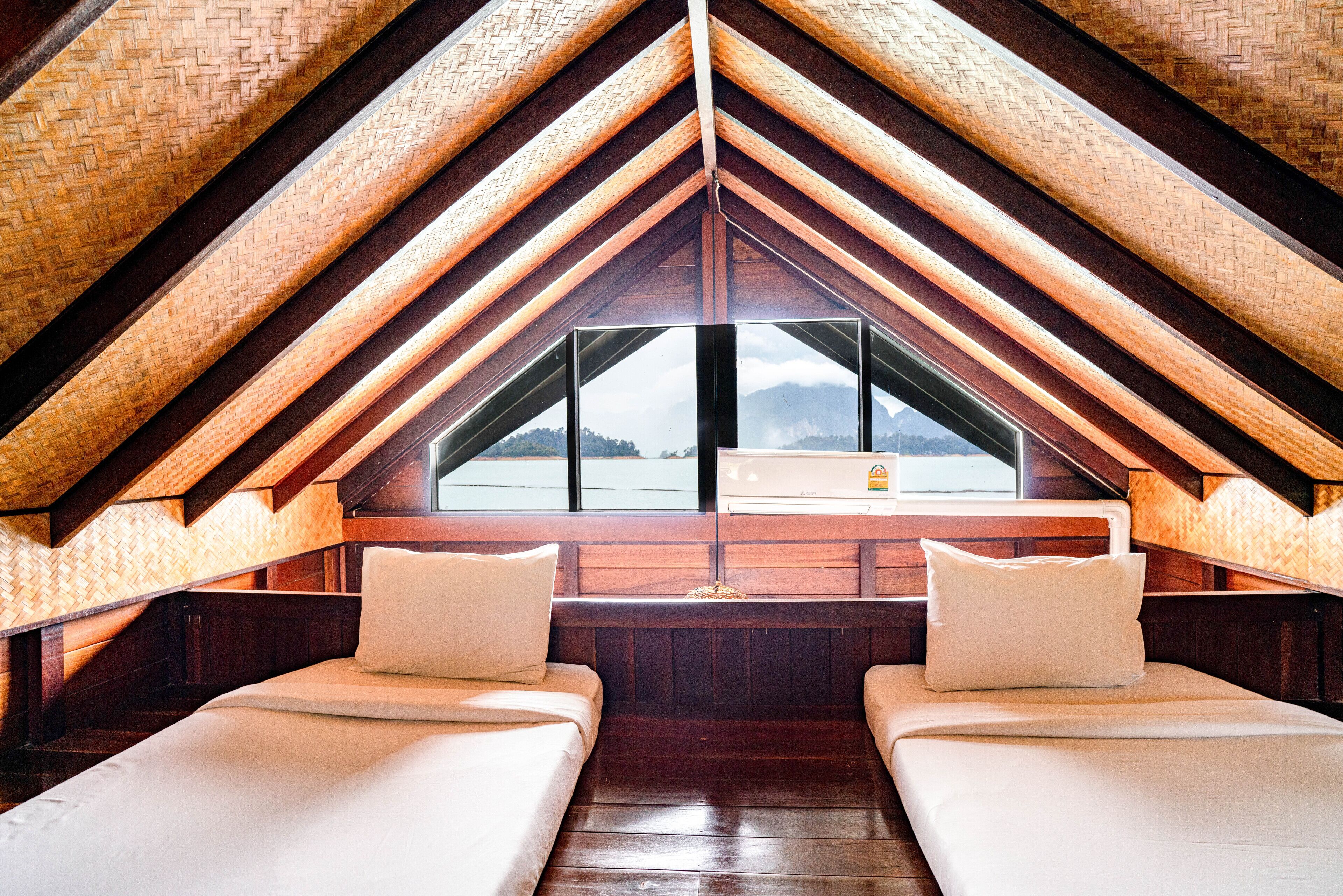 A cozy attic bedroom with two beds, wooden beams, and a large window overlooking a mountainous landscape.