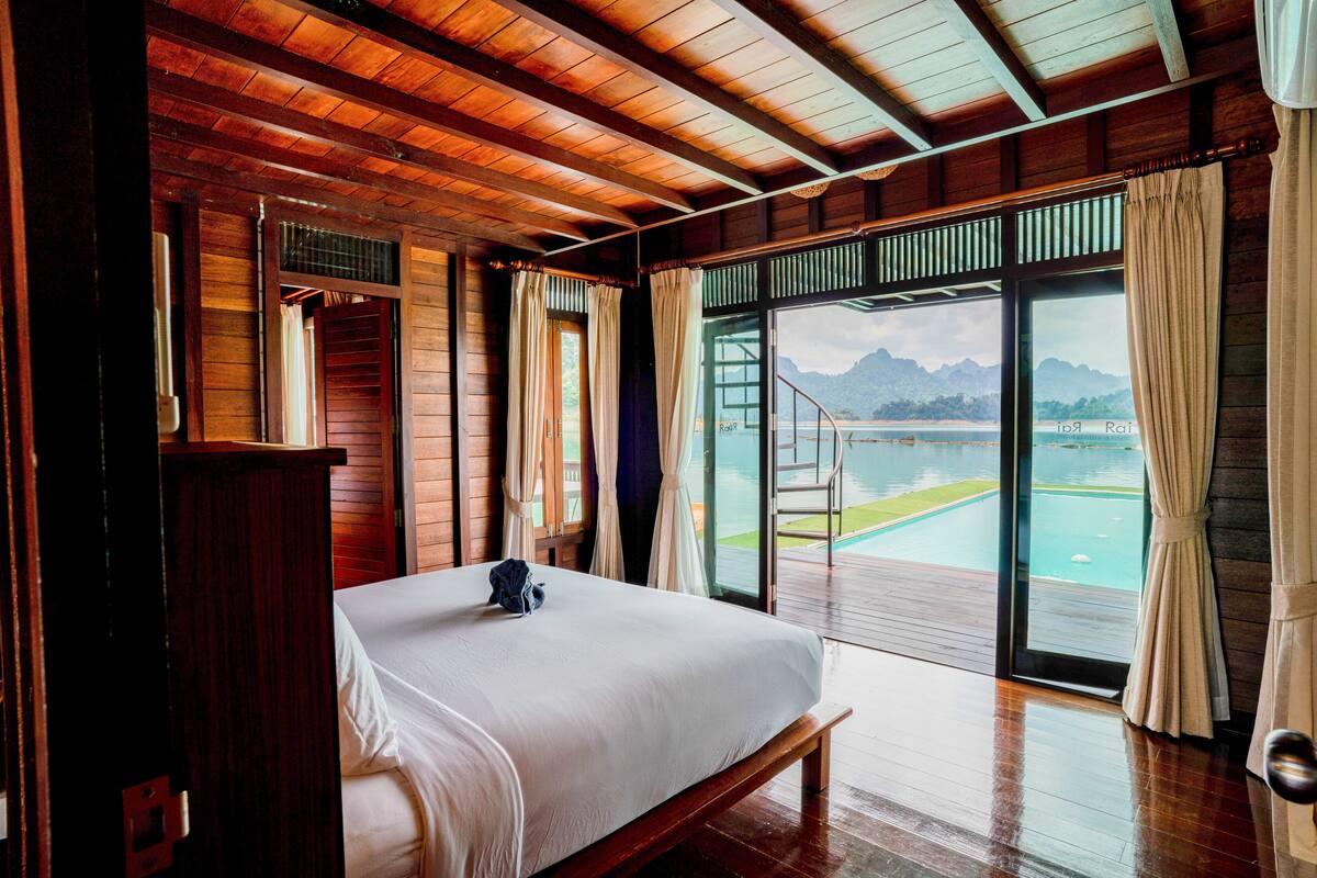 Ein Schlafzimmer mit Holzwandverkleidung, einem großen Bett und Blick auf Pool und Berge durch eine Glastür.