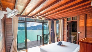 A wooden cabin room with a bed, a ceiling fan, a view of the sea, and a bathroom with a sink. - 500 Rai Khao Sok Floating Resort (Ban Ta Khun)