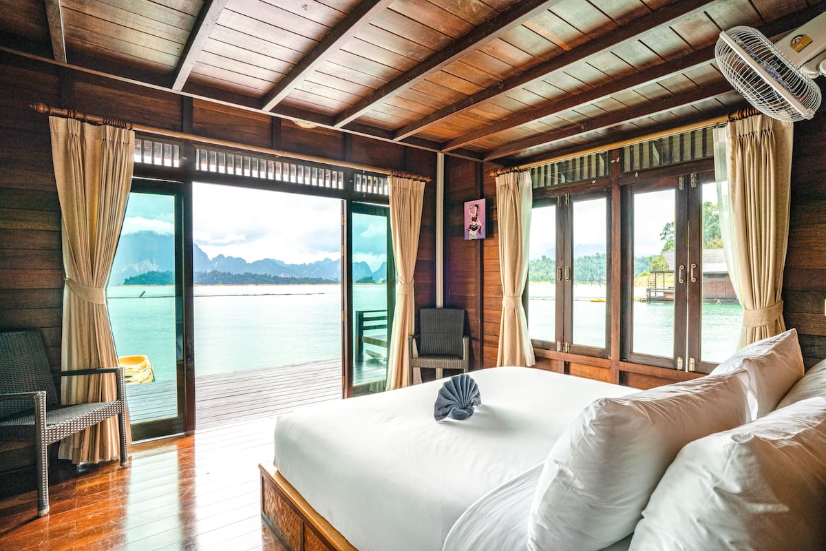 Ein Zimmer in einer Holzhütte mit einem Bett, einem Sessel und Blick auf ein Gewässer.