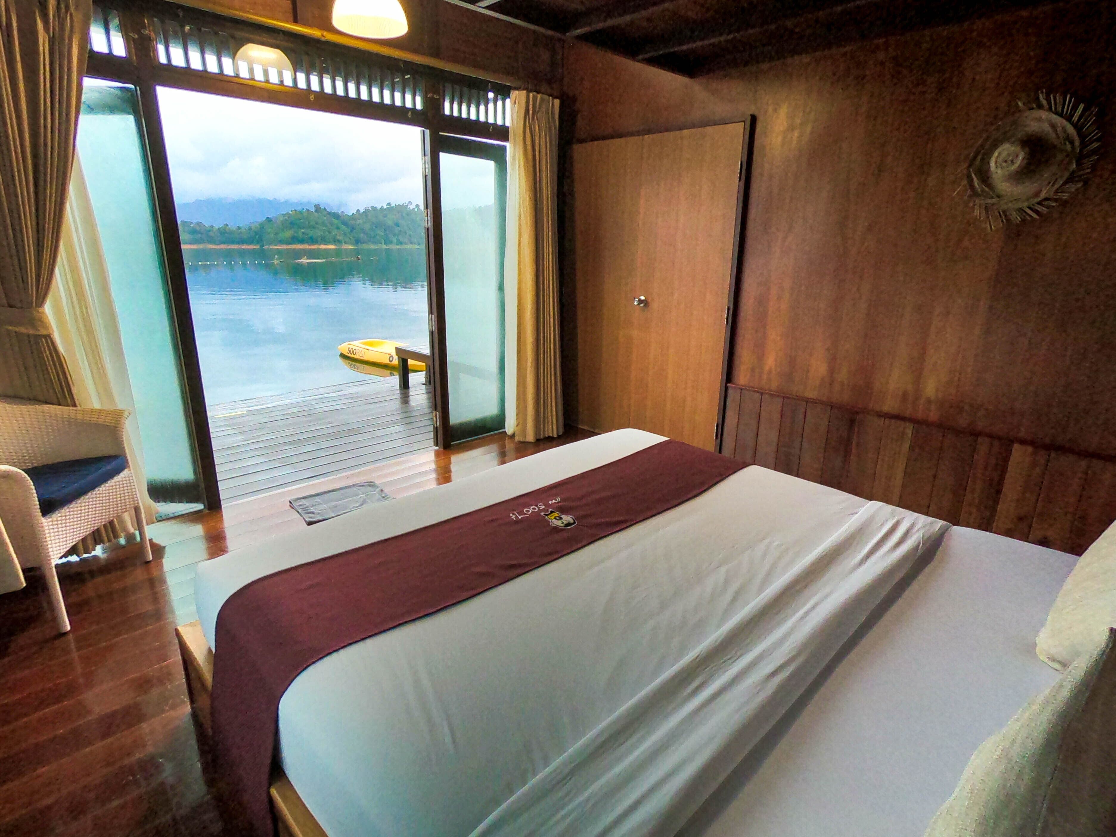 A hotel room with a bed, a chair, a wooden wall, and a view of a body of water through a glass door.