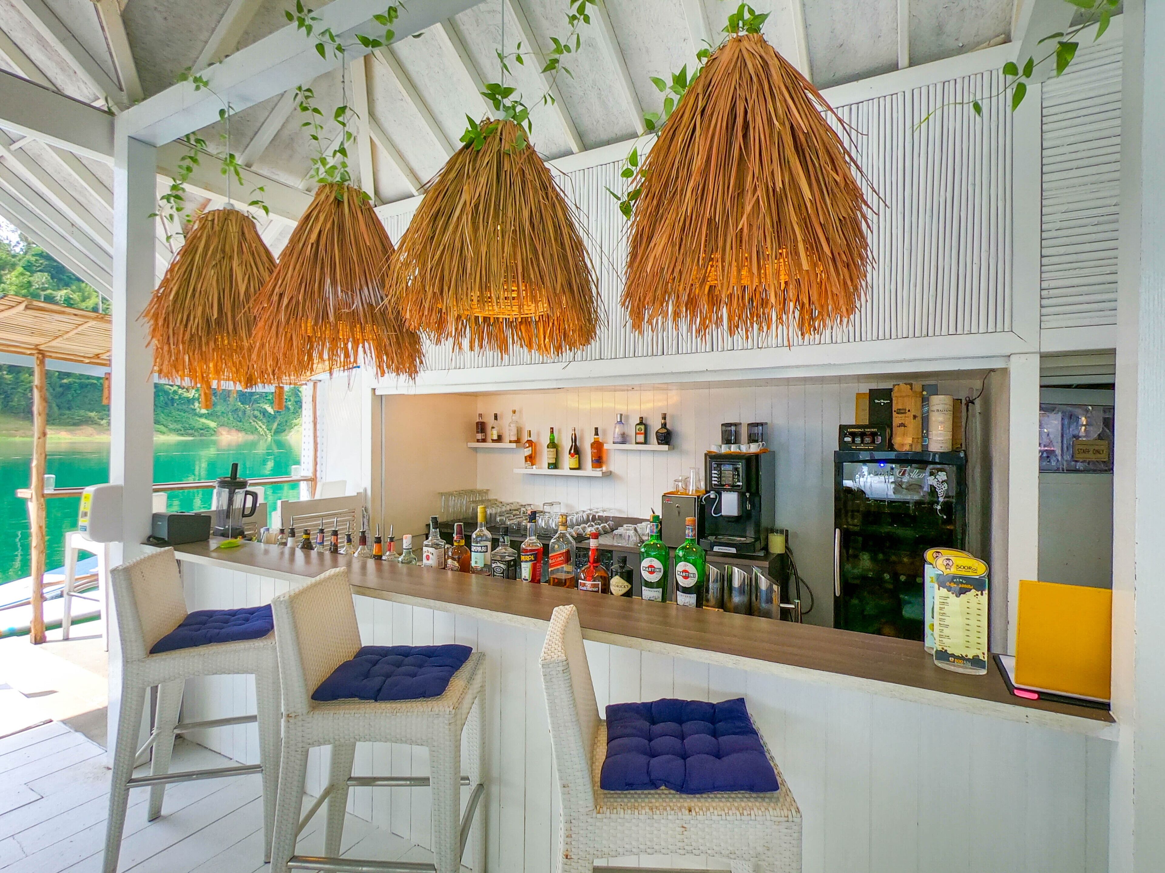 A bar area with wicker chairs and a counter stocked with bottles and a coffee machine.