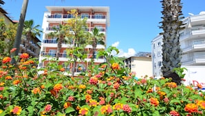 Un hotel a più piani con balconi, immerso nel verde di palme e piante fiorite.