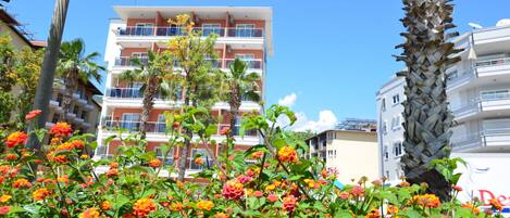 A multi-story hotel with balconies, surrounded by palm trees and flowering plants.