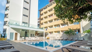 A swimming pool with lounge chairs, a glass balustrade, and a multi-story building with balconies. - Kleopatra Celine Hotel (Alanya)