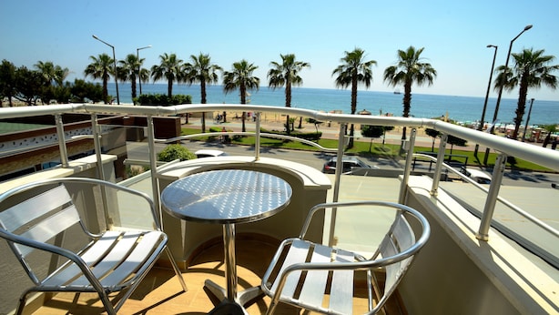 A balcony with two chairs and a table, overlooking a beach with palm trees and a clear sky. - Kleopatra Celine Hotel (Alanya)