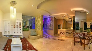 A hotel lobby with a sofa, a coffee table, a reception desk, and a patterned wall. - Kleopatra Celine Hotel (Alanya)