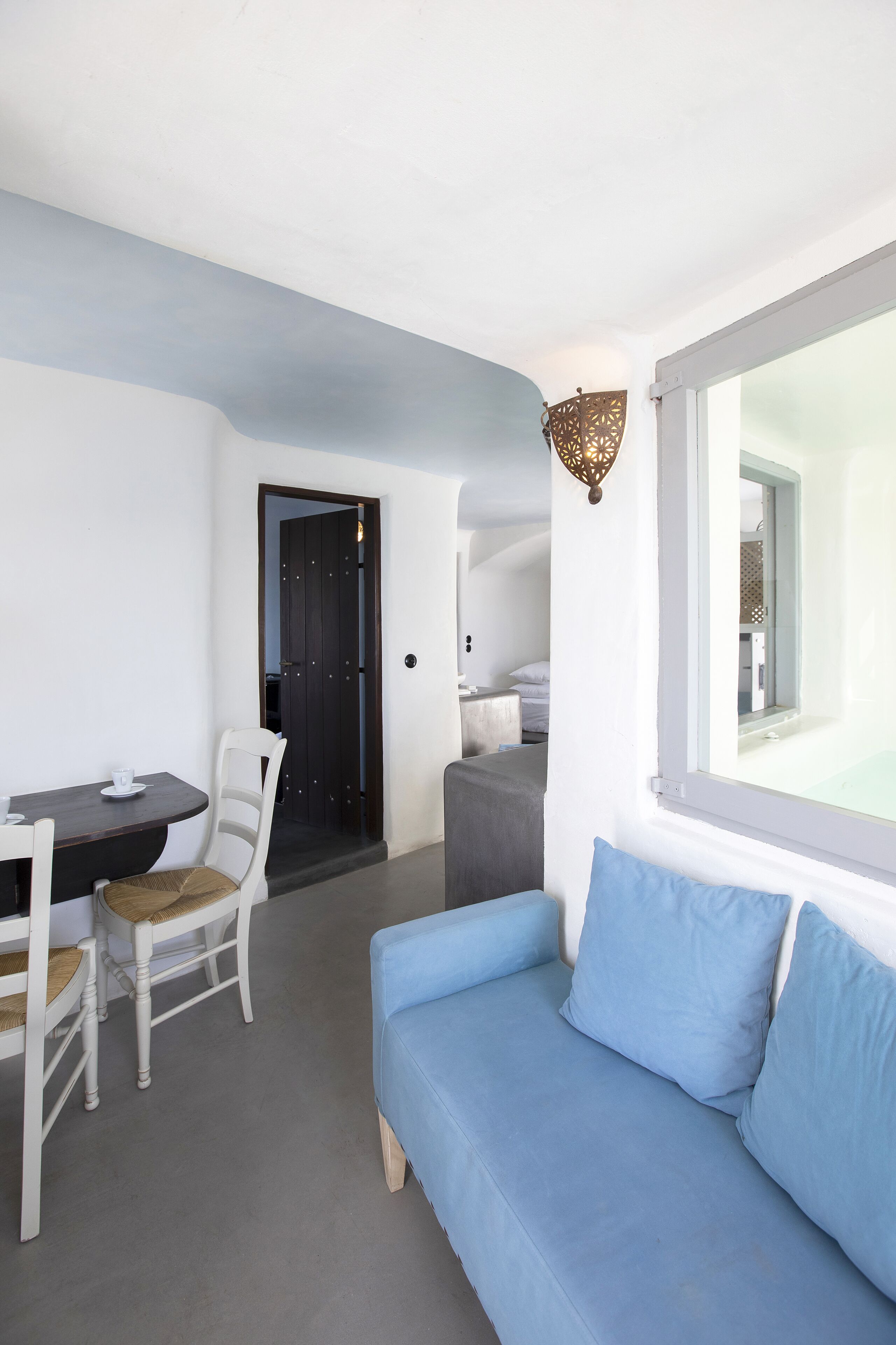 A modern room with a blue sofa, a dining table with chairs, and a large window.