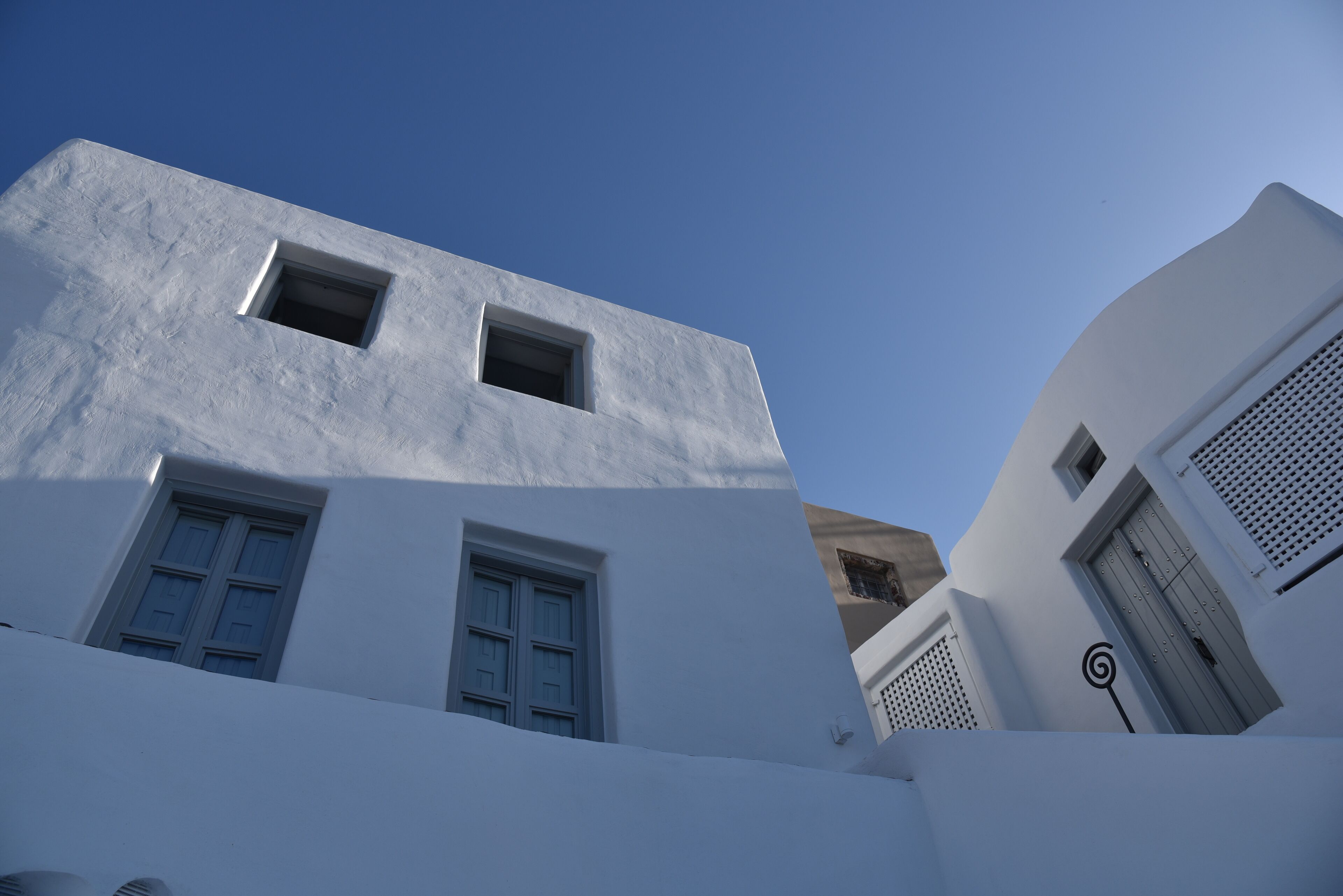 A white building with multiple windows and a door, featuring a clear sky in the background.