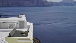 A white building with a flat roof overlooking a calm sea and distant cliffs. - Ducato di Oia - Adults Only (Santorini)