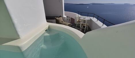 A pool area with a view of the sea and a seating area with a table and chairs.