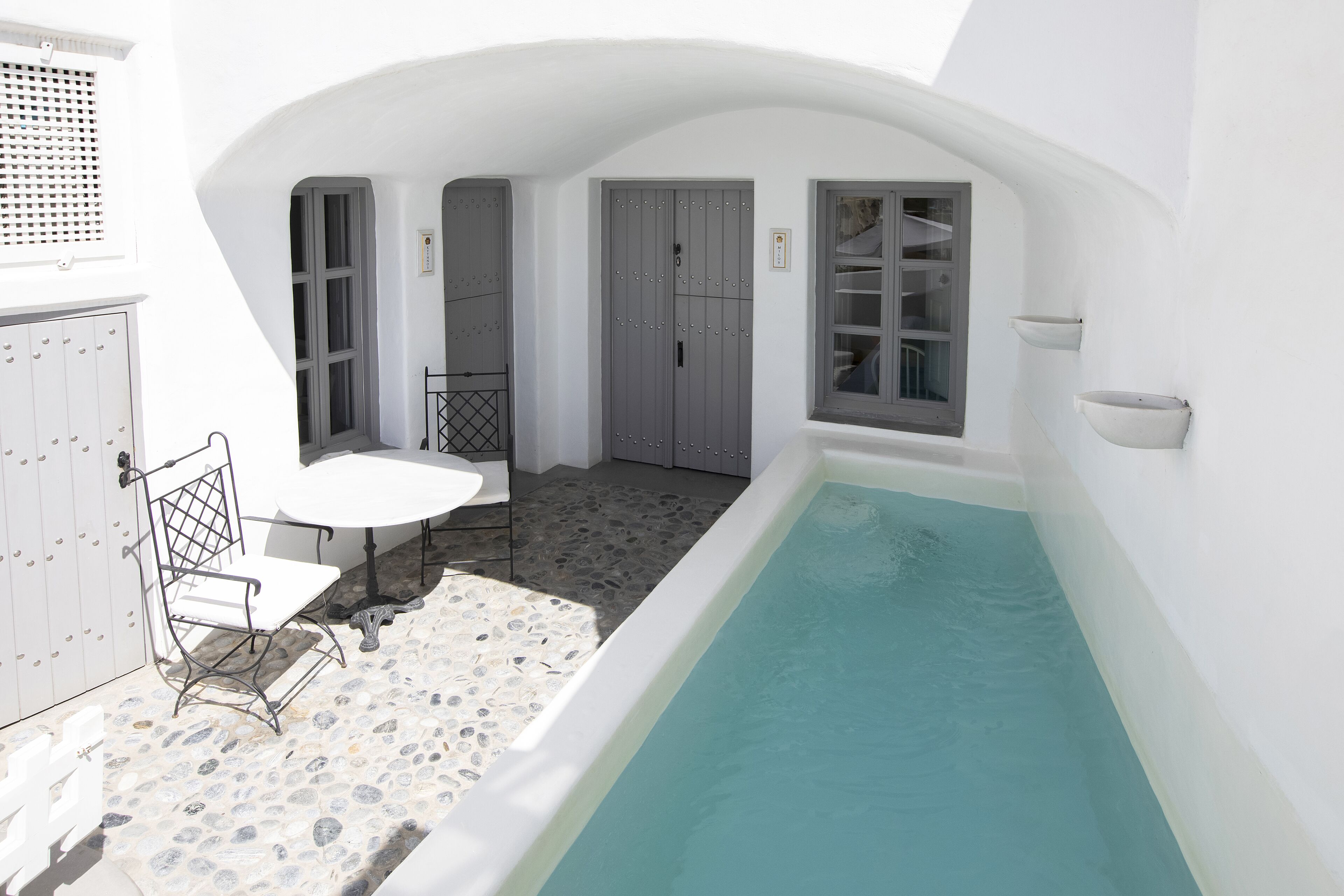 A small, enclosed outdoor area with a pool, a white table, and a chair.