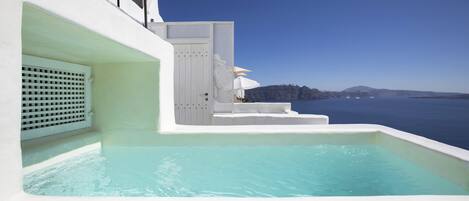 A pool with a view of the sea and a white building with steps leading to a door.