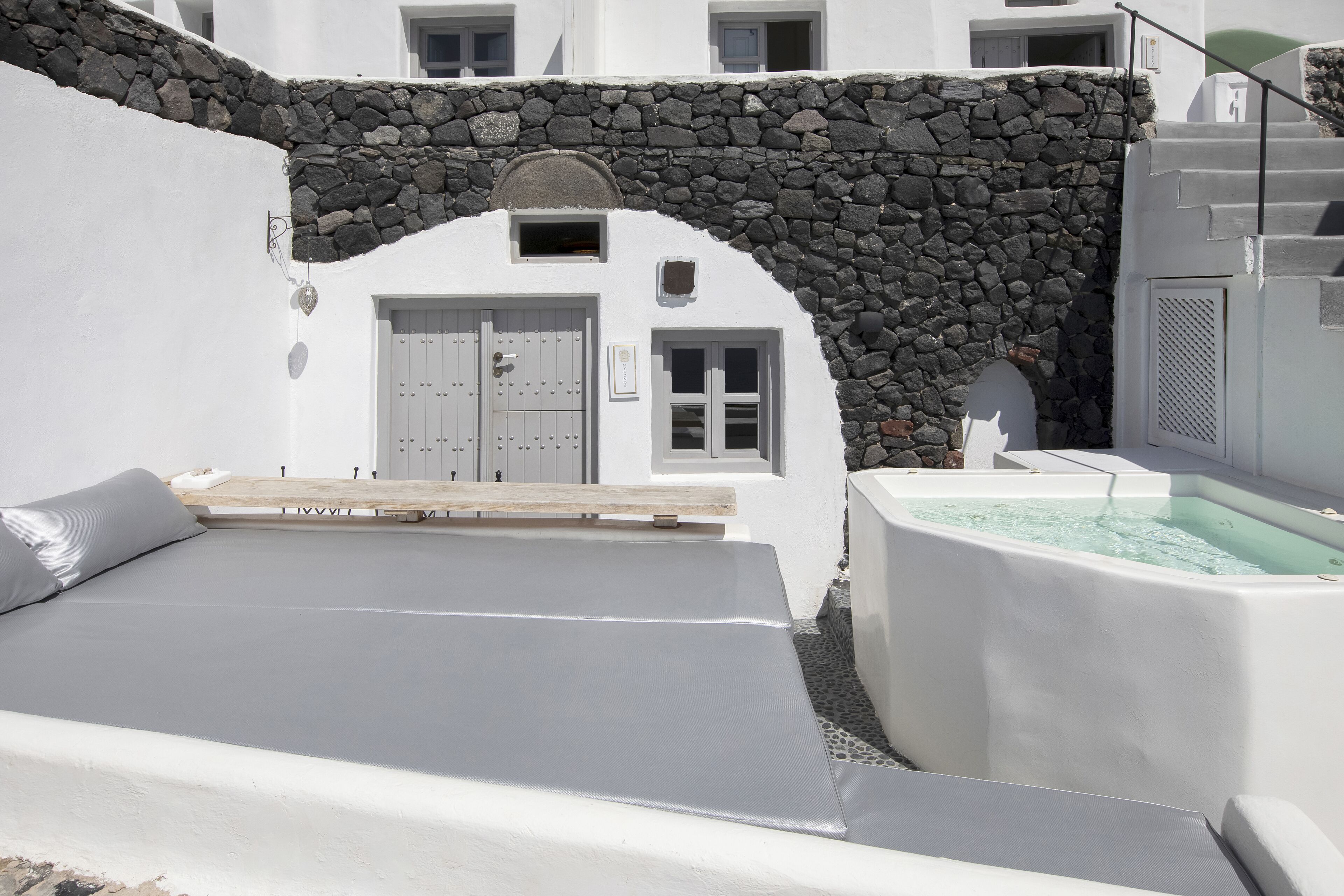 Un edificio blanco con un arco de piedra, un banco de madera y un jacuzzi.