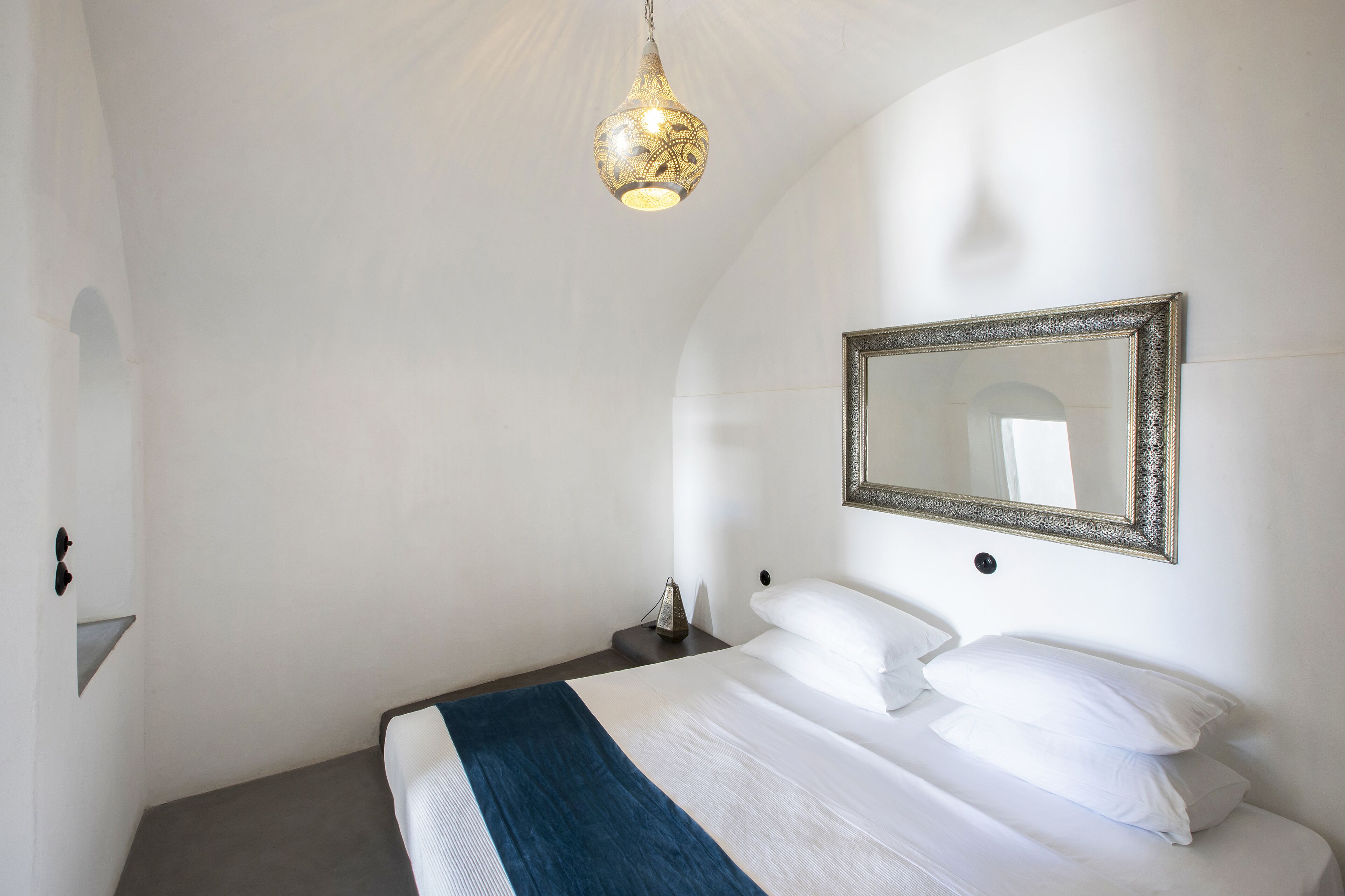 A bedroom with a bed, a bedside table, a lamp, and a mirror on the wall.
