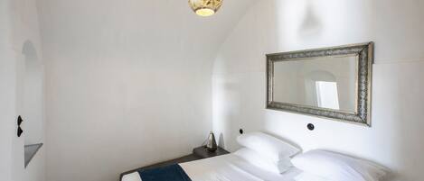 A bedroom with a bed, a bedside table, a lamp, and a mirror on the wall.