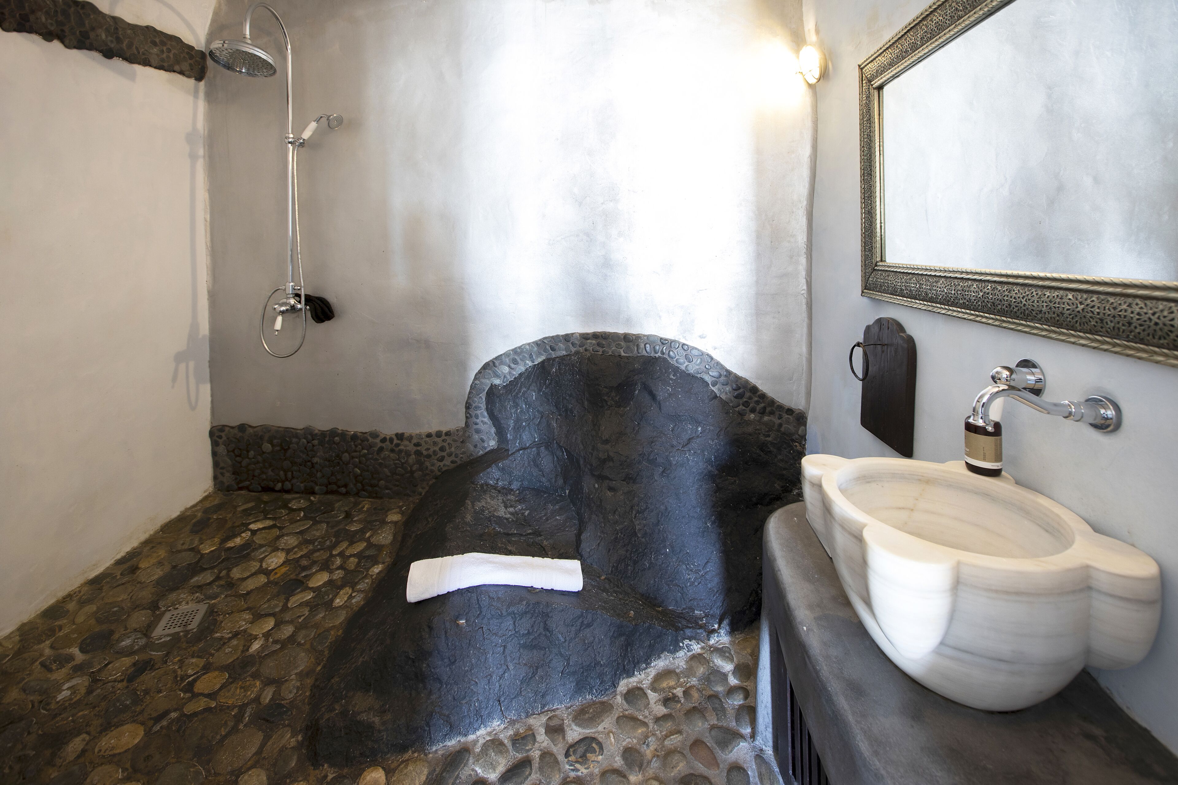Un baño con suelo de piedra, una bañera, un lavabo blanco y una ducha.