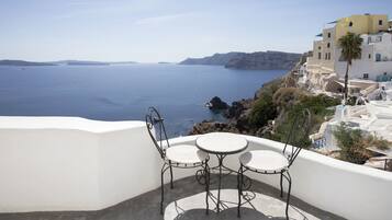 Un balcon avec une table et des chaises donnant sur une vue côtière, avec des bâtiments et des falaises.
