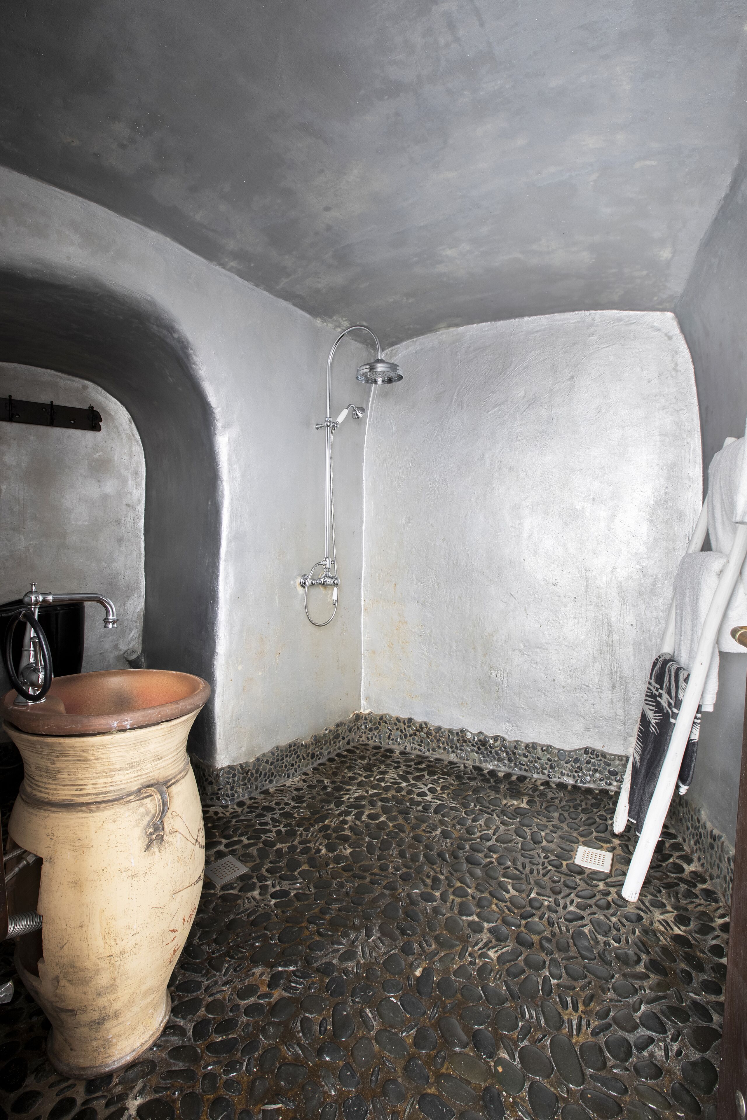 A bathroom with a stone floor, a wooden basin, a shower, and a towel rack.