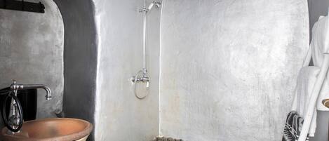 A bathroom with a stone floor, a wooden basin, a shower, and a towel rack.