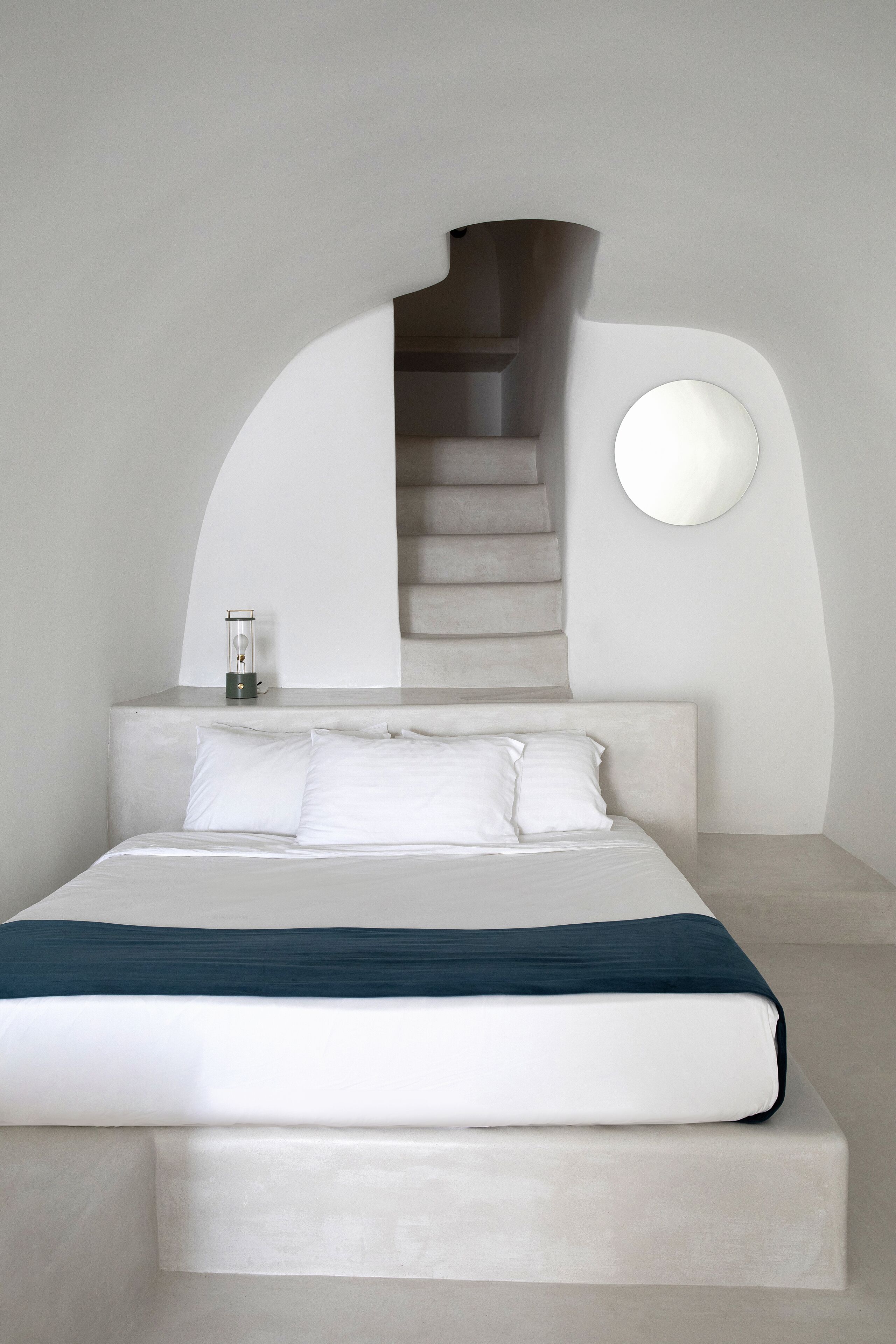 A modern bedroom with a large bed, a glass of water on the nightstand, and a staircase leading to an upper level.