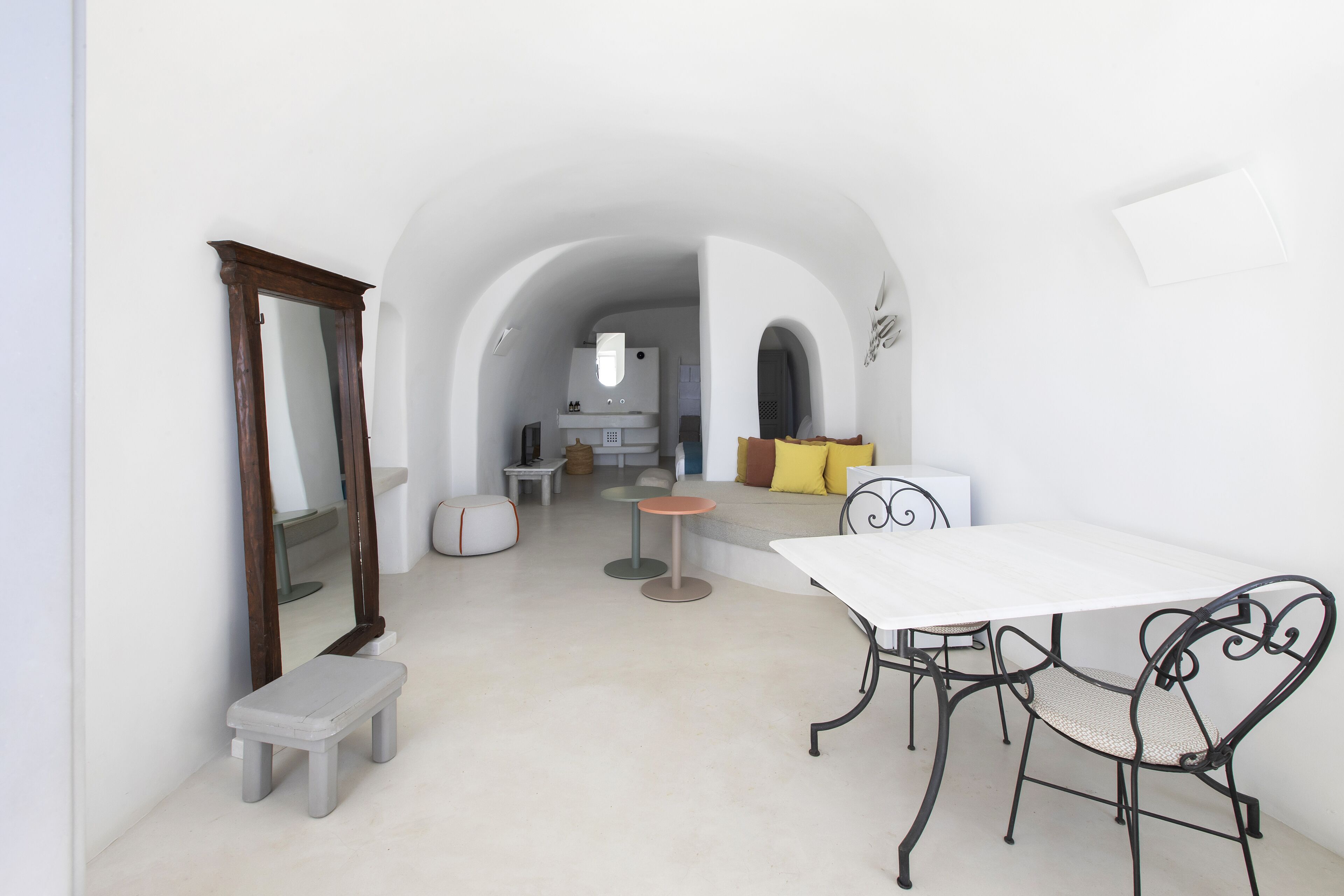 A dining area with a white table and black metal chairs, a small bench, and a mirror on the wall.