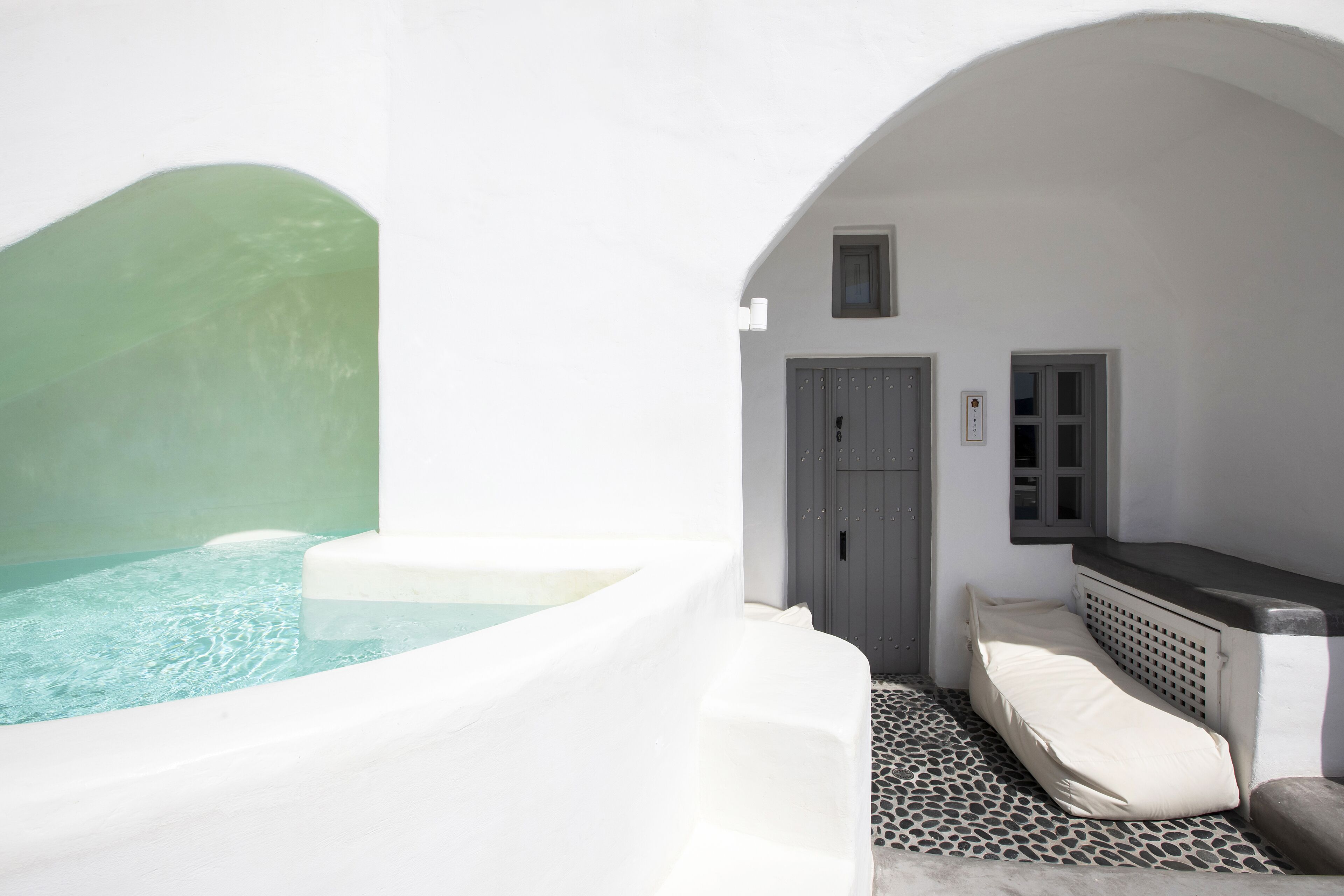 A white, arched bathtub with clear water, a small door, and a bench with cushions.