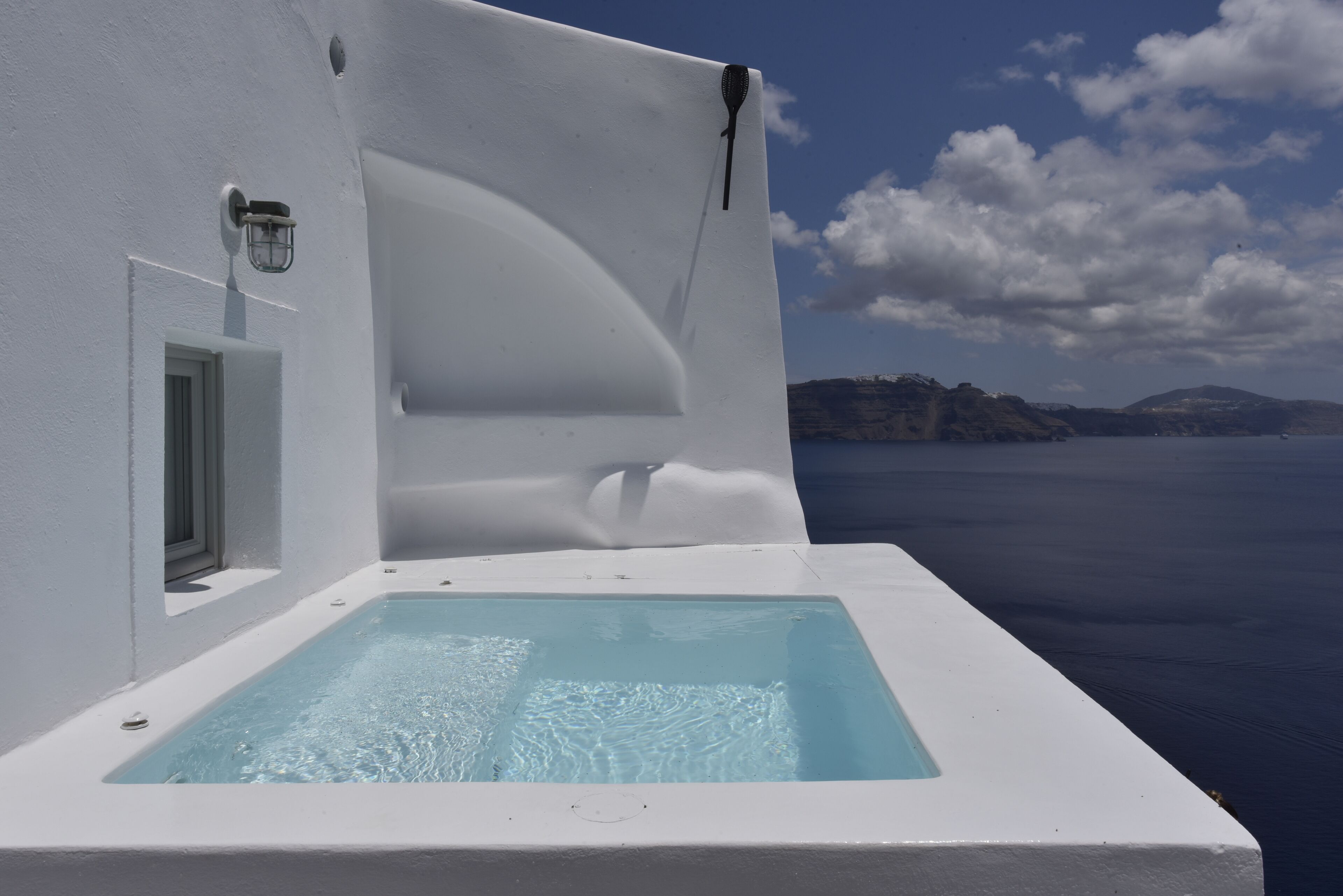 Ein weißer Infinity-Pool mit klarem Wasser, eine Tür und eine Wandleuchte.
