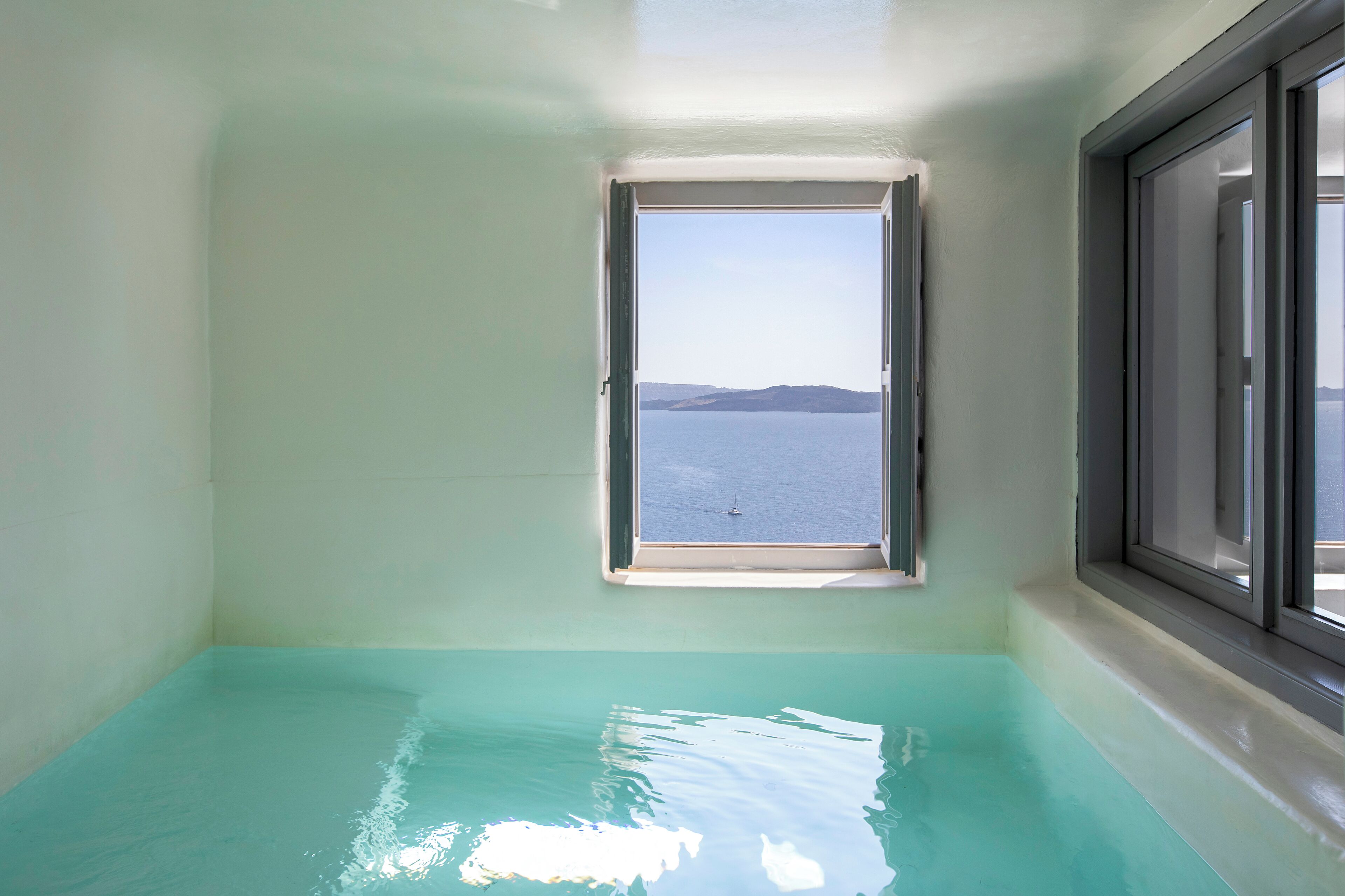 A room with a small window overlooking a body of water and a distant landmass.