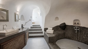 A modern bathroom with a stone sink, a large bathtub, and a staircase leading to a bright room. - Ducato di Oia - Adults Only (Santorini)